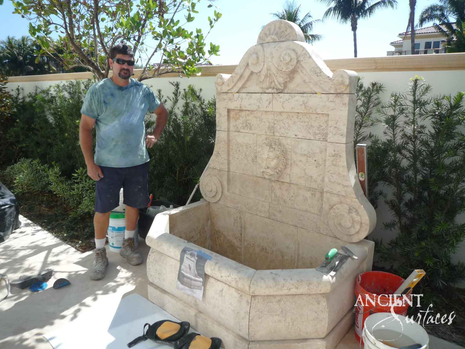 Cream limestone wall fountain with a carved shell crest and lion mascaron installed in a garden